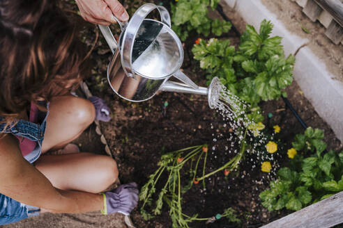 Woman crouching by man watering plants in community garden - EBBF00421