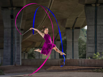 Junge Frau hält Bänder, während sie unter einer Brücke rhythmische Gymnastik macht - STSF02564