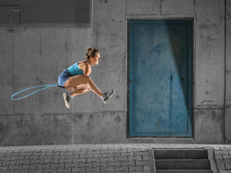 Junge Frau springt über Springseil gegen Betonwand unter Brücke - STSF02568
