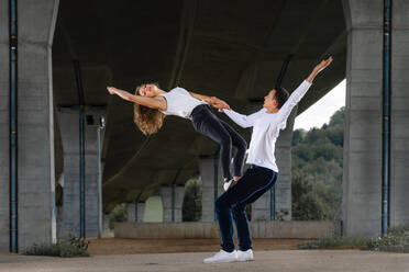 Male and female friends practicing aerobics on road under bridge - STSF02572