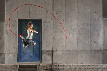 Frau, die ein Band hält, übt rhythmische Gymnastik gegen eine Mauer unter einer Brücke - STSF02576