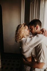 Seitenansicht eines Paares, das sich zu Hause umarmt und aneinander hängt. - ADSF01490