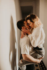 Side view of passionate man and woman embracing and kissing at wall in the hall at home. - ADSF01504