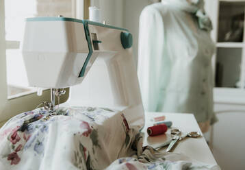 Schaufensterpuppe mit eleganter Jacke steht neben einem Tisch mit moderner Nähmaschine und Fenster in einer Schneiderei - ADSF01624