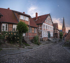 Deutschland, Schleswig-Holstein, Lauenburg, Häuser entlang einer leeren Kopfsteinpflasterstraße in der Abenddämmerung - HAMF00679