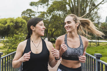 Smiling female friends jogging in park - DSIF00042