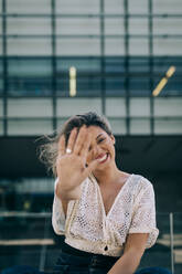 Fröhliche Frau zeigt ihre Handfläche gegen ein Gebäude - DCRF00425