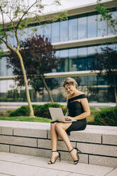 Businesswoman working on laptop outdoors - DCRF00452