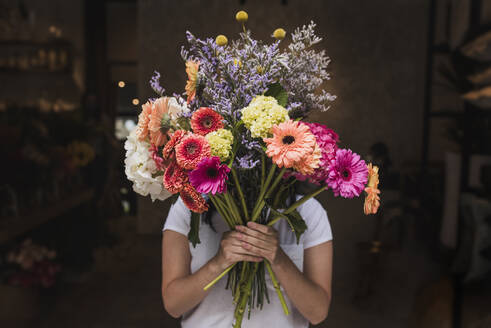 Female florist holding colorful flowers while standing in shop - DSIF00053