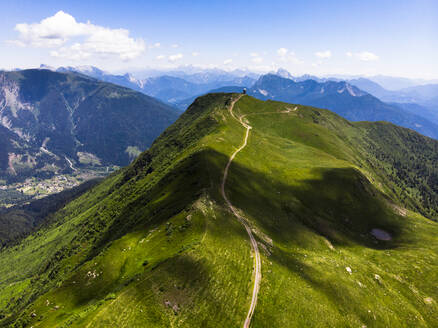 Italy, Friuli Venezia Giulia, Aerial view of dirt road stretching along green peak in Italian Alps - GIOF08593