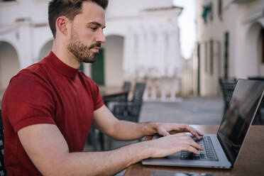 Mann mit Laptop auf Tisch in der Stadt - GRCF00276