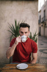 Man drinking coffee at sidewalk cafe - GRCF00296