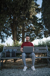 Geschäftsmann, der einen Laptop benutzt, während er auf einer Bank im Park sitzt - GRCF00301