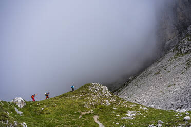 Male hikers walking on mountain during foggy weather at Bergamasque Alps, Italy - MCVF00532