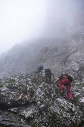 Mature men climbing on mountain during foggy weather, Bergamasque Alps, Italy - MCVF00535