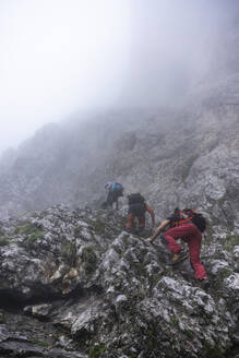 Ältere Männer klettern bei nebligem Wetter auf einen Berg, Bergamasker Alpen, Italien - MCVF00535