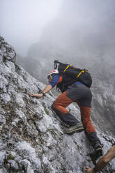 Mature male hiker climbing on mountain during foggy weather, Bergamasque Alps, Italy - MCVF00537