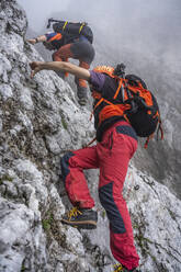 Ältere Männer beim Klettern auf einem felsigen Berg bei nebligem Wetter, Bergamasker Alpen, Italien - MCVF00538