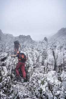 Männliche Wanderer klettern auf felsigem Berg gegen den Himmel bei nebligem Wetter, Bergamasker Alpen, Italien - MCVF00539