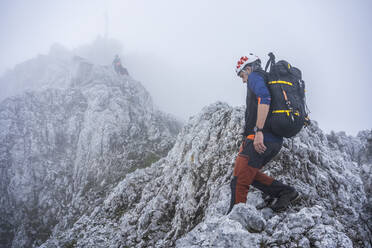 Ältere Männer wandern auf felsigen Bergen gegen den Himmel bei nebligem Wetter, Bergamasker Alpen, Italien - MCVF00540