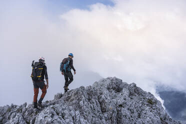 Ältere Männer wandern auf einem Berg gegen den bewölkten Himmel, Bergamasker Alpen, Italien - MCVF00541
