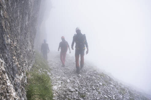 Ältere Männer wandern bei nebligem Wetter auf einem Berg, Bergamasker Alpen, Italien - MCVF00544