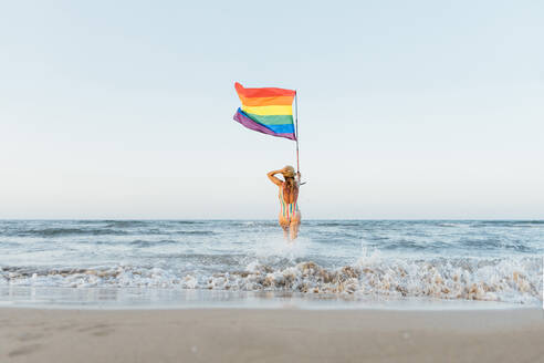 Reife Frau am Strand mit Homosexuell Stolz Flagge, Rückansicht - CJMF00306