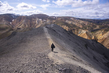 Man with cape walking down trail on top of mountain in Iceland - CAVF87192