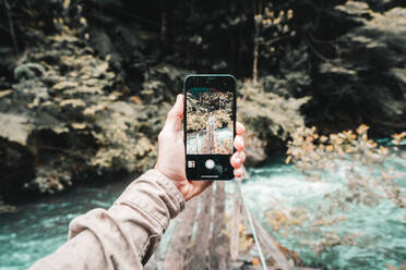 FPV - Hiker photographing footbridge over river with smart phone - CAVF87222