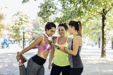 Lächelnde junge Freundinnen in Sportkleidung mit Smartphone im Park - CAVF87261