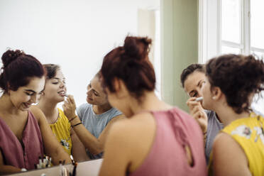 Fröhliche, unterschiedliche Frauen, die sich zu Hause gemeinsam schminken - CAVF87275