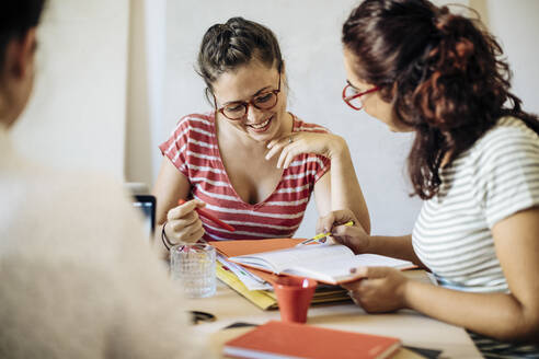 Lächelnde, lässige Frauen, die am Schreibtisch über Geschäftsstrategien diskutieren - CAVF87280