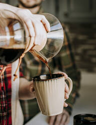 Hot coffee is poured from a pour over into a tan coffee cup - CAVF87333