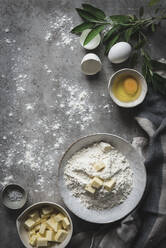 Flat lay of beautiful arrangement with bowl of flour and butter with eggs on marble table with green branch - ADSF01637