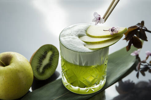 Kristallglas mit servierten Getränken in grüner Farbe serviert mit Apfelscheiben und kleinen Blumen auf dem Tisch mit grünen Früchten - ADSF01654