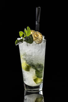 High glass with traditional Mojito cocktail garnished with dried lime and mint on black background - ADSF01656