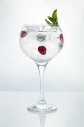 Kristall Weinglas mit Eis gefüllt und Getränk mit reifen Himbeeren garniert mit Minze auf weißem Hintergrund - ADSF01658