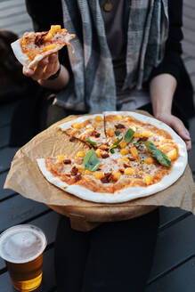 Gesichtslose Aufnahme einer Frau, die mit einer Tasse Bier und einer gebackenen Pizza auf einem Podium sitzt - ADSF01666