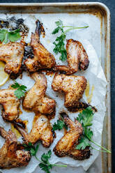 From above shot of baking tray with parchment and baked chicken wings in sesame and parsley with lemon - ADSF01684