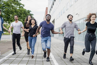 Fröhliche männliche und weibliche Freunde halten sich an den Händen und laufen auf einem Fußweg in der Stadt - MEUF01501