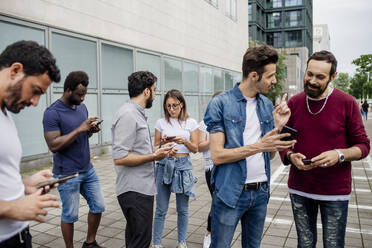 Freunde unterhalten sich und benutzen Smartphones, während sie auf einem Fußweg in der Stadt stehen - MEUF01515