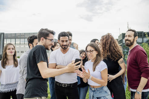 Glücklicher Mann zeigt Freunden im Park sein Smartphone - MEUF01527