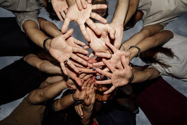 Group of friends stacking hands against sky in park at sunset - MEUF01530