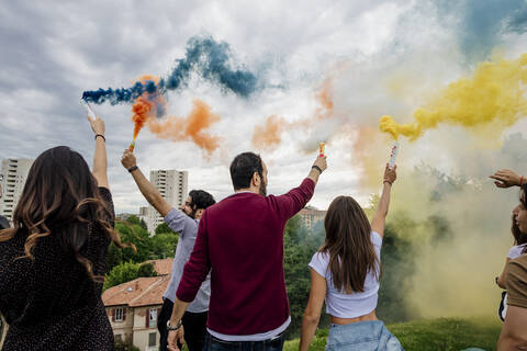 Männliche und weibliche Freunde spielen mit Rauchbomben im Park am Wochenende, lizenzfreies Stockfoto