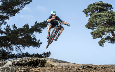 Mountain biker performing jump on bicycle on single track in forest - ADSF01736