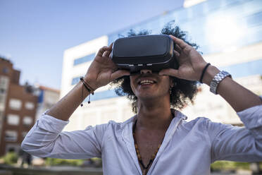 Attraktiver Latino-Mann mit Afro-Haar, der sein Virtual-Reality-Gerät auf der Straße genießt - ADSF01756