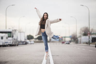 Woman dancer on one ballet tips, jeans and white coat on the street - ADSF01780