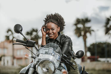 Schöne afroamerikanische Dame lächelnd und Blick auf die Kamera, während auf wunderbare moderne Motorrad auf unscharfen Hintergrund der Stadt Straße sitzen - ADSF01792