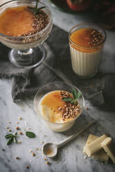 Pieces of white chocolate and small spoon lying on marble tabletop near glasses with delicious panna cotta - ADSF01797