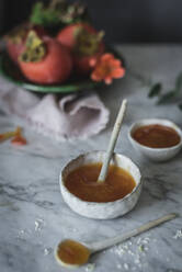 Small spoon lying in bowl with fresh honey for panna cotta on marble tabletop - ADSF01800